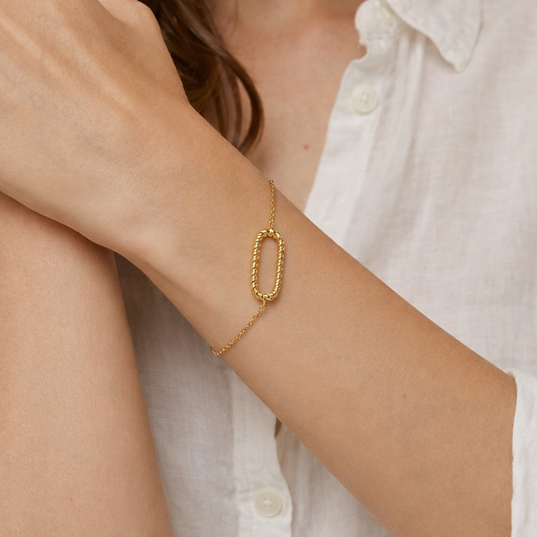 femme portant un Bracelet fin en métal doré composé d’une chaîne délicate avec au centre un motif ovale torsadé.